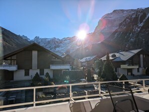 Une station de montagne avec des bâtiments de style chalet, un balcon avec un fauteuil et une vue dégagée sur les montagnes enneigées.