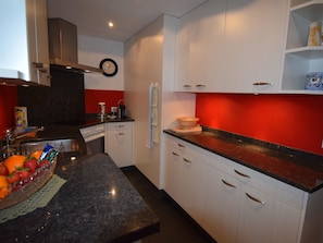 Una cucina moderna con mobili bianchi, un piano di lavoro in granito e una parete di accento rossa.