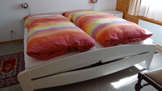 Una cama blanca con almohadas a rayas de arcoíris en una habitación con suelo de madera y una alfombra estampada.