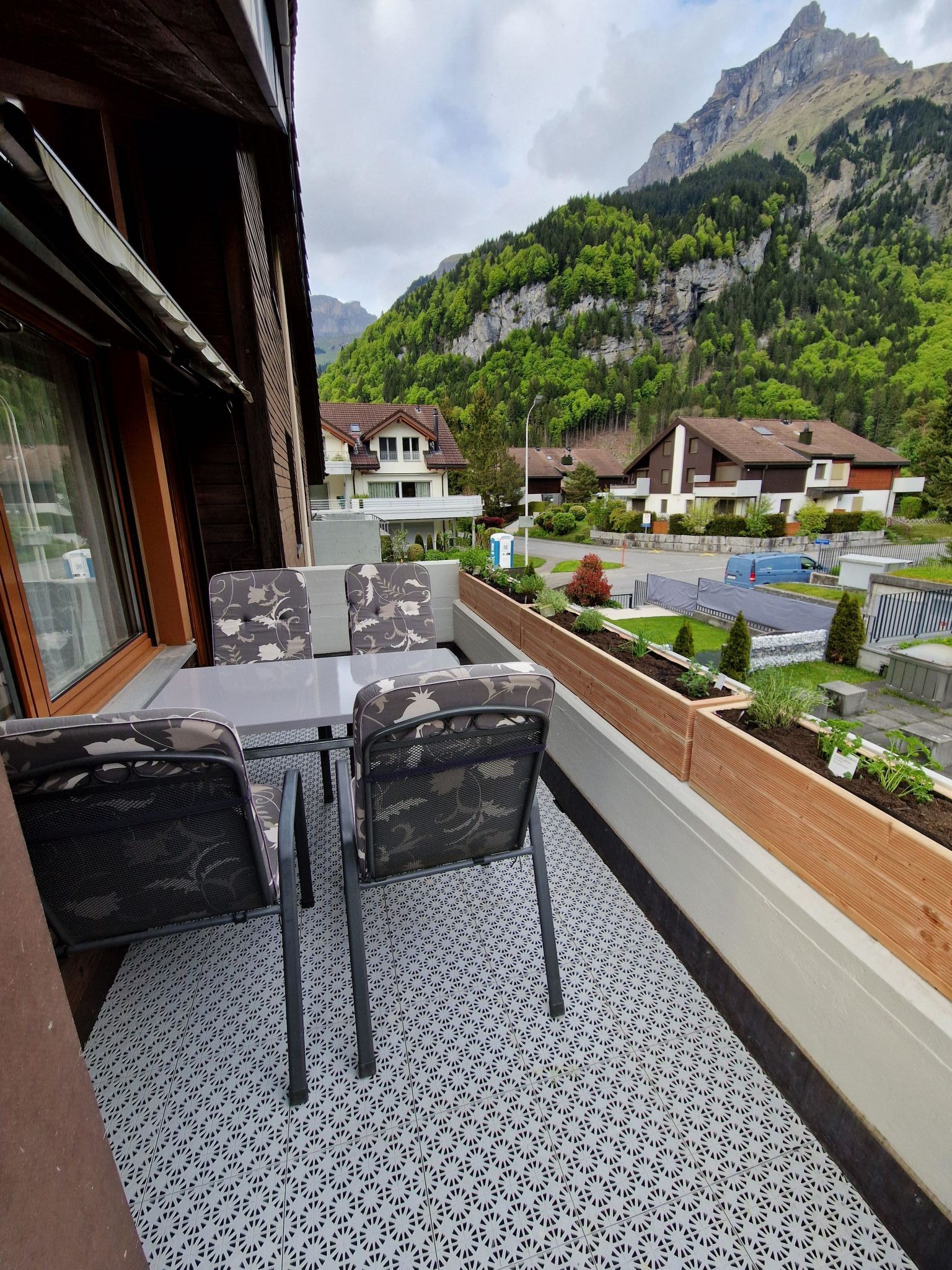 Een balkon met buitenmeubilair, uitzicht op een berg en woongebouwen op de achtergrond.