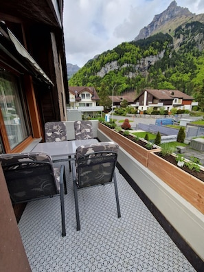 A balcony with outdoor seating, a view of a mountain, and residential buildings in the background.