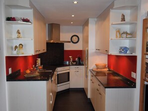 Cocina compacta con armarios blancos, encimera negra y pared roja de acento.