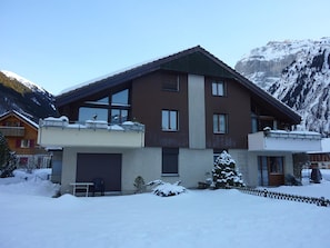 Una casa a due piani con un balcone, un garage e una montagna innevata sullo sfondo.