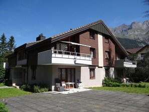 Una casa a due piani con un balcone, vialetto e montagne sullo sfondo.