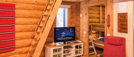 A wooden cabin interior with a TV, a red chair, and a wooden ladder.