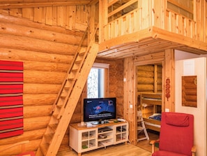 Interior de una cabaña de madera con televisión, un sillón rojo y una escalera de madera.