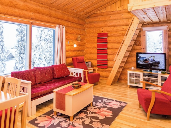 Un interior acogedor de cabaña de troncos con un sofá, sillones, un televisor y una chimenea.