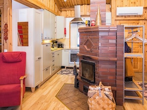 Interior acogedor de una cabaña con chimenea, paredes de madera, una silla roja y una zona de cocina.