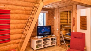 A log cabin interior with a wooden staircase, a television, and a red chair.