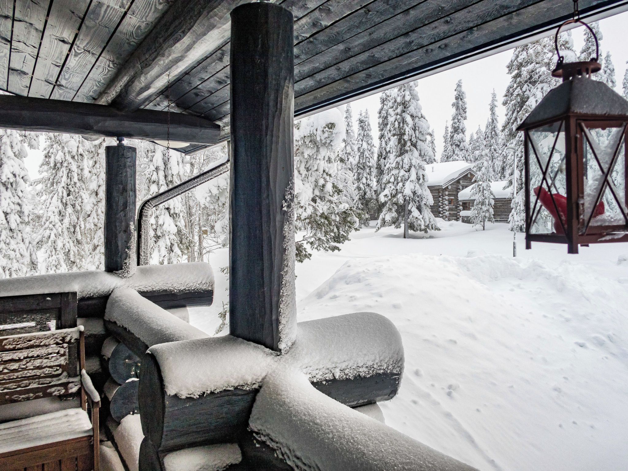 A wooden cabin with a snow-covered deck and a view of a snow-covered forest.