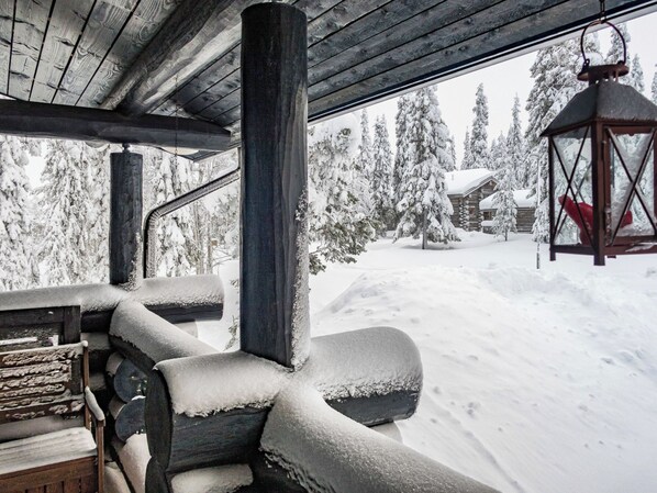 A wooden cabin with a snow-covered deck and a view of a snow-covered forest.