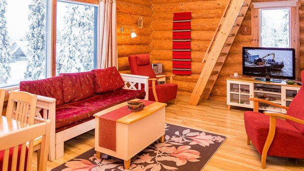 A cozy log cabin interior with a sofa, chairs, a TV, and a wooden staircase.