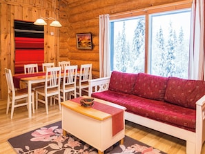 Interior acogedor de una cabaña con una mesa de comedor, sillas, un sofá y un amplio ventanal con vistas nevadas.