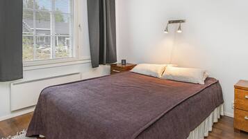 A bedroom with a bed, a nightstand, a wall-mounted light fixture, and a window with blinds.