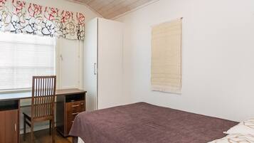 A bedroom with a bed, a desk with a chair, a wardrobe, and a window with blinds.
