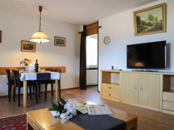 A living room with a dining table, chairs, a TV, and a wooden cabinet.
