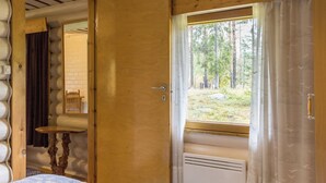 A cozy cabin room with a bed, a window with curtains, a wooden door, and a small table.