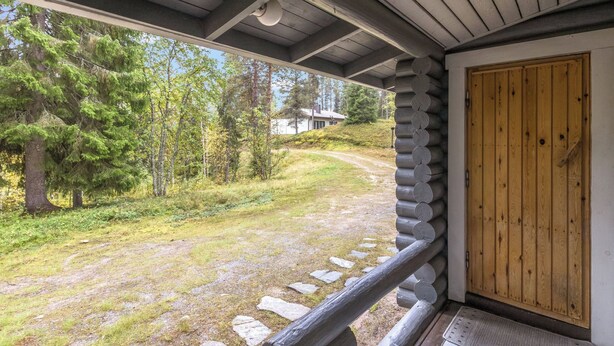A cabin with a wooden door and a porch overlooking a grassy area with trees.
