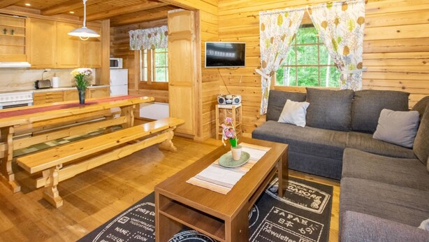 A cozy cabin-style room with wooden walls and floors, a sofa, a dining table, a TV, and a kitchen area. - Meritähti by Interhome (Pöytyä)
