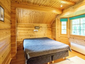 En stuga med träpanel, ett rum med en säng, ett fönster och en väggmonterad värmare.