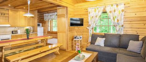 Interior acogedor de una cabaña con paredes de madera, un comedor con bancos, un sofá y un televisor.
