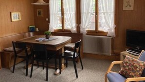 A cozy room with a wooden ceiling, a dining table with chairs, a radiator, and a television.