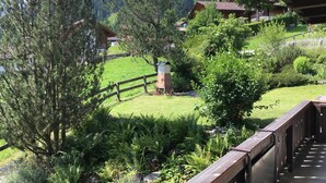 A view of a lush garden with a wooden deck overlooking a green landscape and houses.