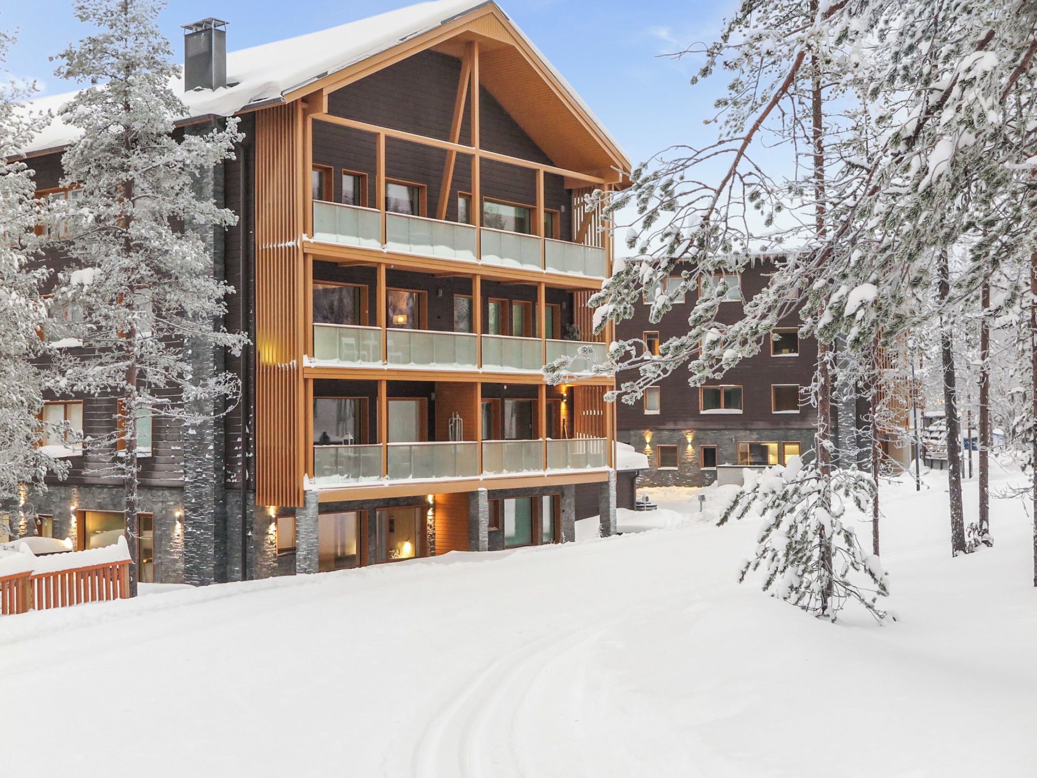 A multi-story wooden building with balconies, surrounded by snow-covered trees.