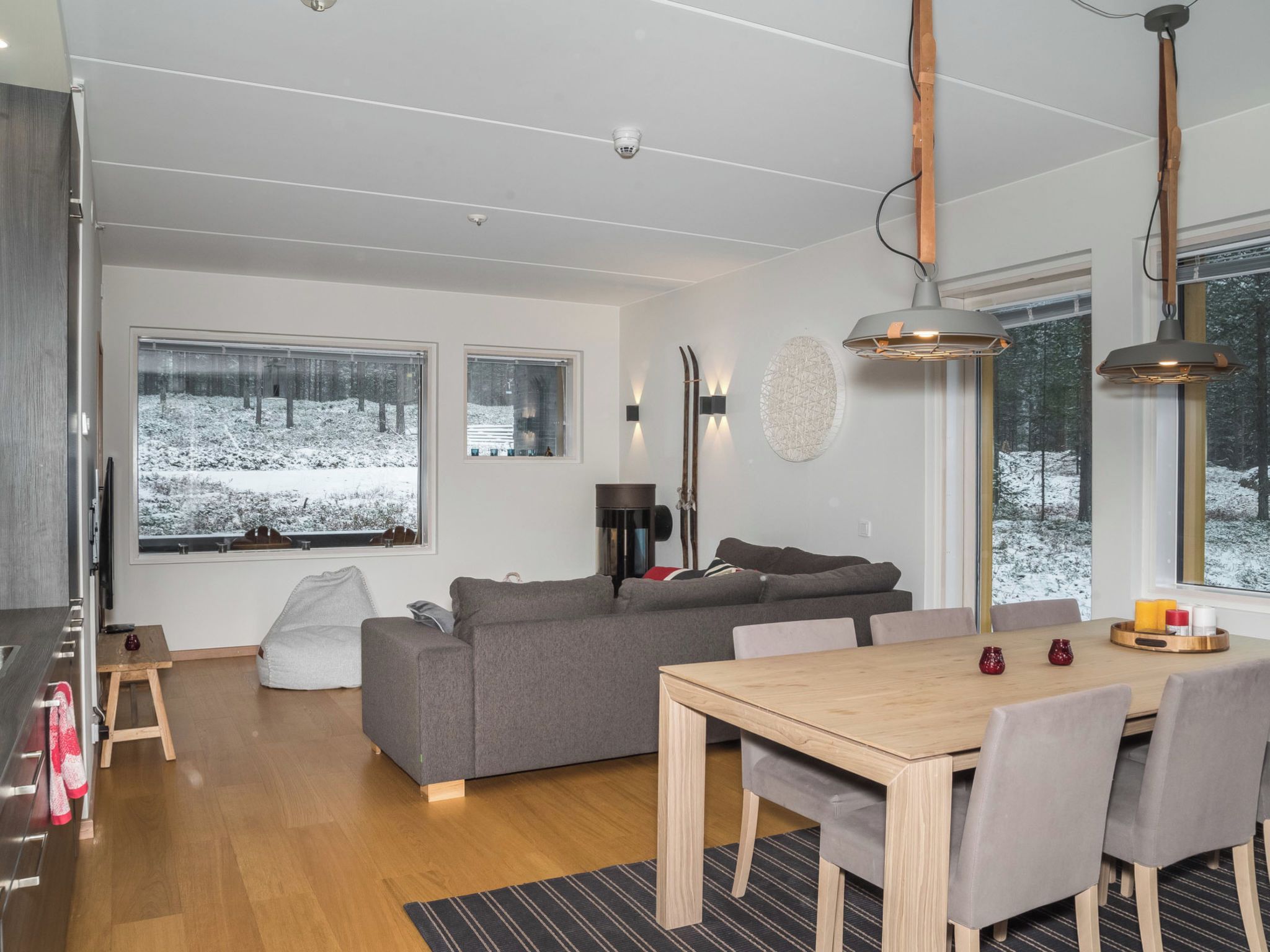 Un salon moderne avec un canapé gris, une table à manger en bois et de grandes fenêtres offrant une vue sur un paysage enneigé.