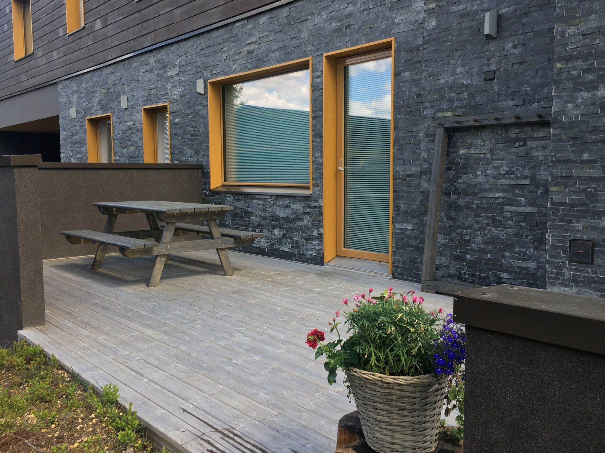 A modern building with a wooden deck, a picnic table, and a potted plant with flowers.