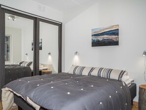 Quarto com cama grande, espelho, pintura e luminárias de cabeceira.