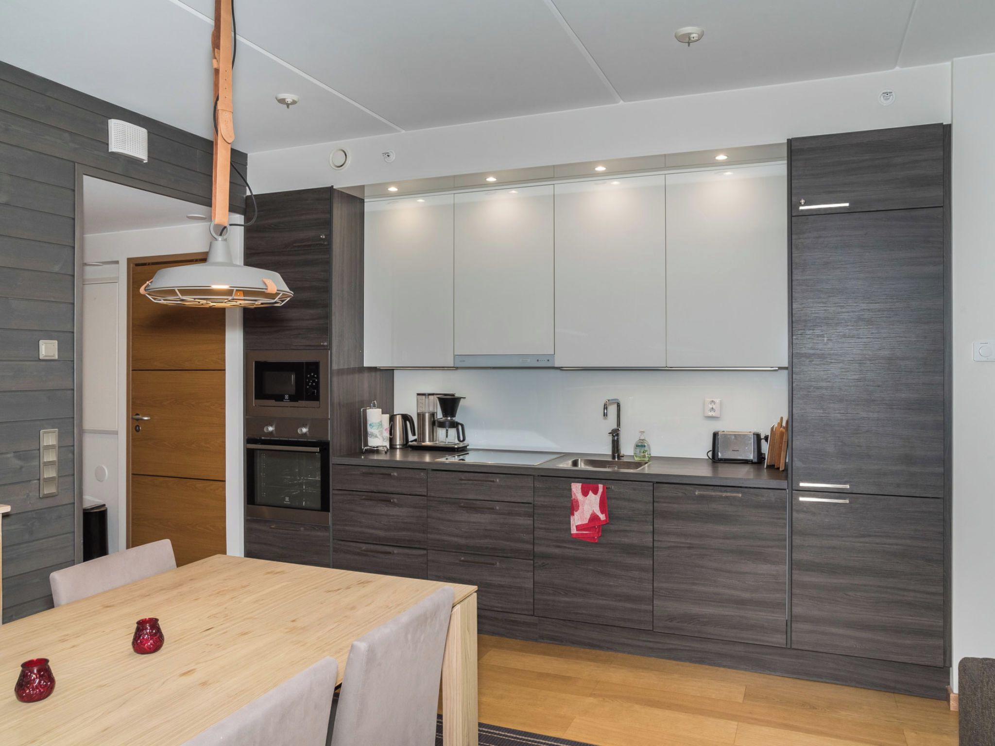 Una cocina moderna con armarios de madera oscura, horno empotrado, cafetera y lavamanos.