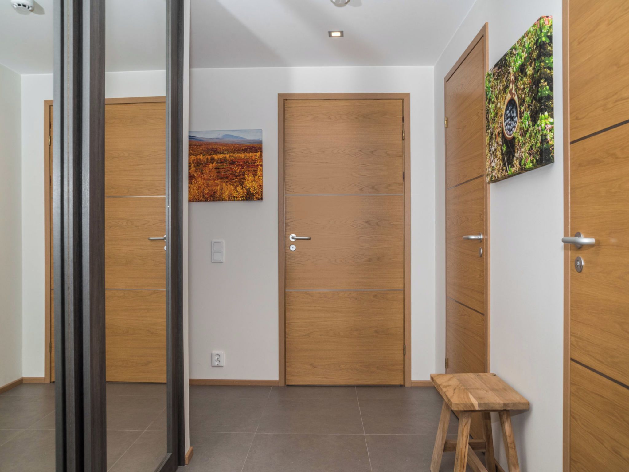 A hallway with wooden doors, a small stool, and a painting on the wall.