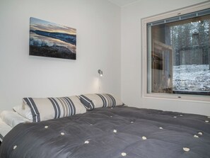 A bedroom with a large bed, a window with a view of a snowy forest, and a painting on the wall.