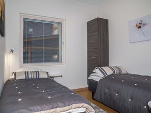 Une chambre avec deux lits, une fenêtre avec des stores, une armoire et un tableau au mur.