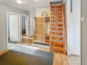 Un pasillo con una escalera de madera, un armario con almacenamiento vertical y una puerta que da a otra habitación.