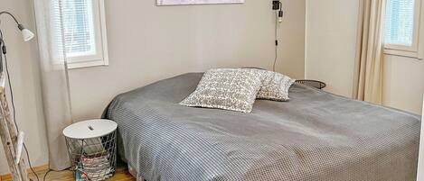 Un dormitorio con cama, mesita de noche, lámpara, luz de pared y ventana con persianas.