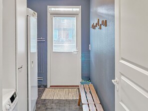 Un pasillo con una puerta, una ventana con persianas, un radiador, un banco y una pared con textura.