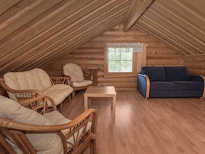 Une pièce mansardée chaleureuse aux murs en bois et aux plafonds inclinés, aménagée avec des fauteuils en osier, un canapé bleu et une petite table en bois.