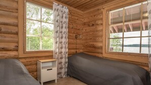 A cabin-style room with two beds, a small white nightstand, and large windows with blinds. - Juusola by Interhome (Ikaalinen)