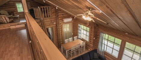 A log cabin interior with a dining area, sofa, and a staircase leading to an upper level.