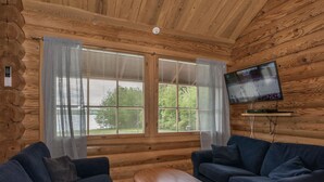 A log cabin interior with two sofas, a coffee table, a TV mounted on the wall, and large windows with blinds. - Juusola by Interhome (Ikaalinen)