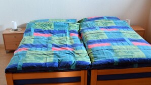 A double bed with a colorful quilt, a wooden nightstand with a lamp, and a small drawer. - Matten EG Süd by Interhome (Ried-Mörel)