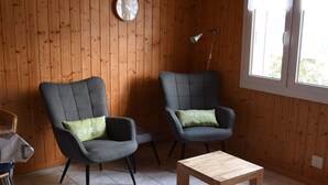 A room with two grey armchairs, a wooden table, a clock, and a window with natural light. - Matten EG Süd by Interhome (Ried-Mörel)