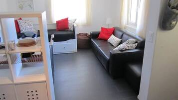 Un salon moderne avec un canapé en cuir noir, un meuble blanc avec rangements et une fenêtre avec des rideaux.