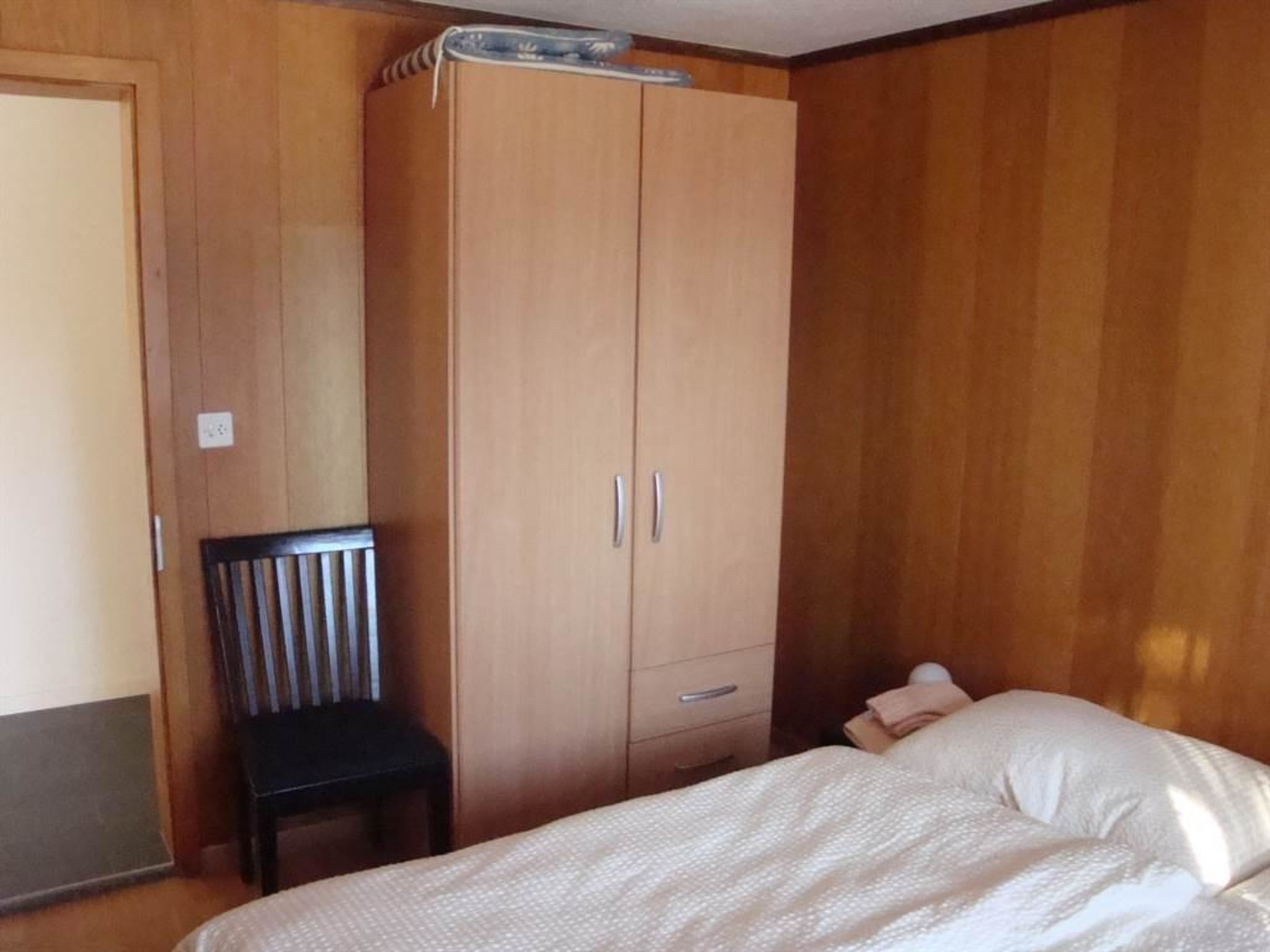Ein Schlafzimmer mit einem Bett, einem Holzschrank und einem Stuhl.