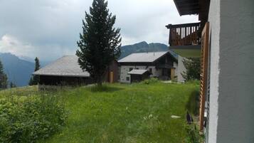 Une maison de campagne dotée d’un toit en pente, entourée d’une végétation luxuriante et avec des montagnes en toile de fond.