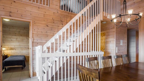A wooden cabin interior with a staircase, a dining area, and a bed.
