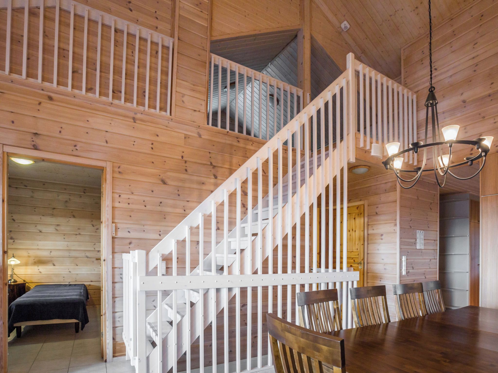 A wooden interior with a staircase, a dining area with chairs, and a chandelier.