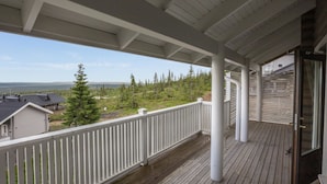 A wooden deck with a white railing overlooking a forested landscape.